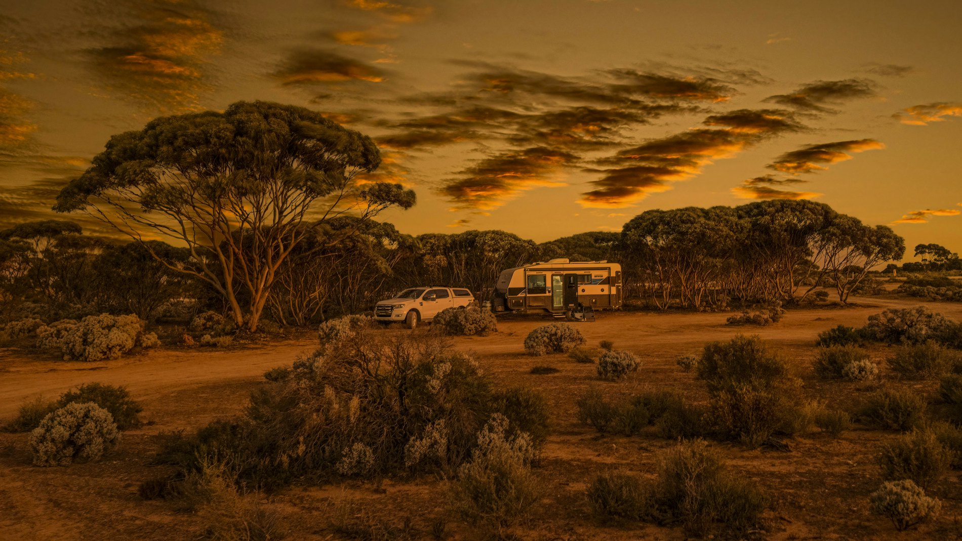 A four-wheel drive and caravan camped in the Australian outback at sunset